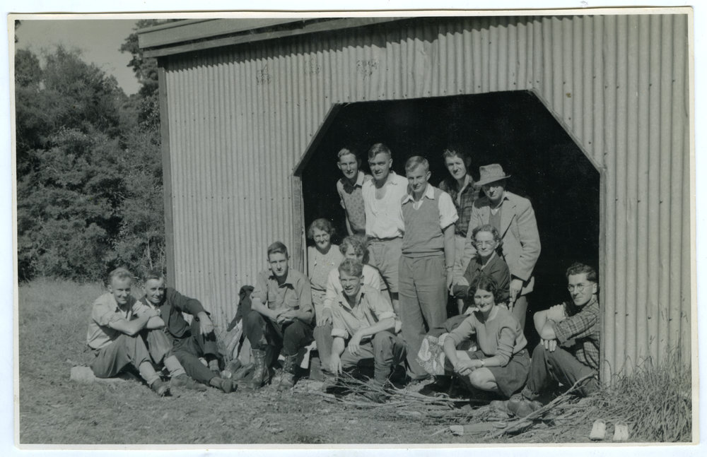 A group of unidentified men and women seated around an entrance to a barn