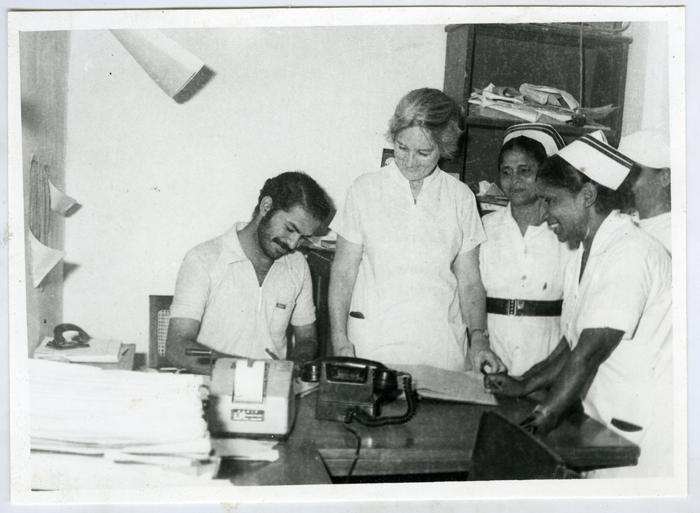Beryl Howie stands over the shoulder of an Indian orderly, whilst two unidentified Indian nurses look on
