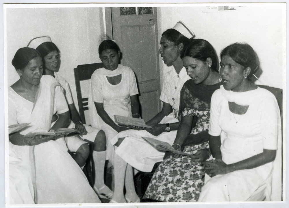 Six unidentified Indian women are seated in a circle, reading a pamphlet, Ludhiana