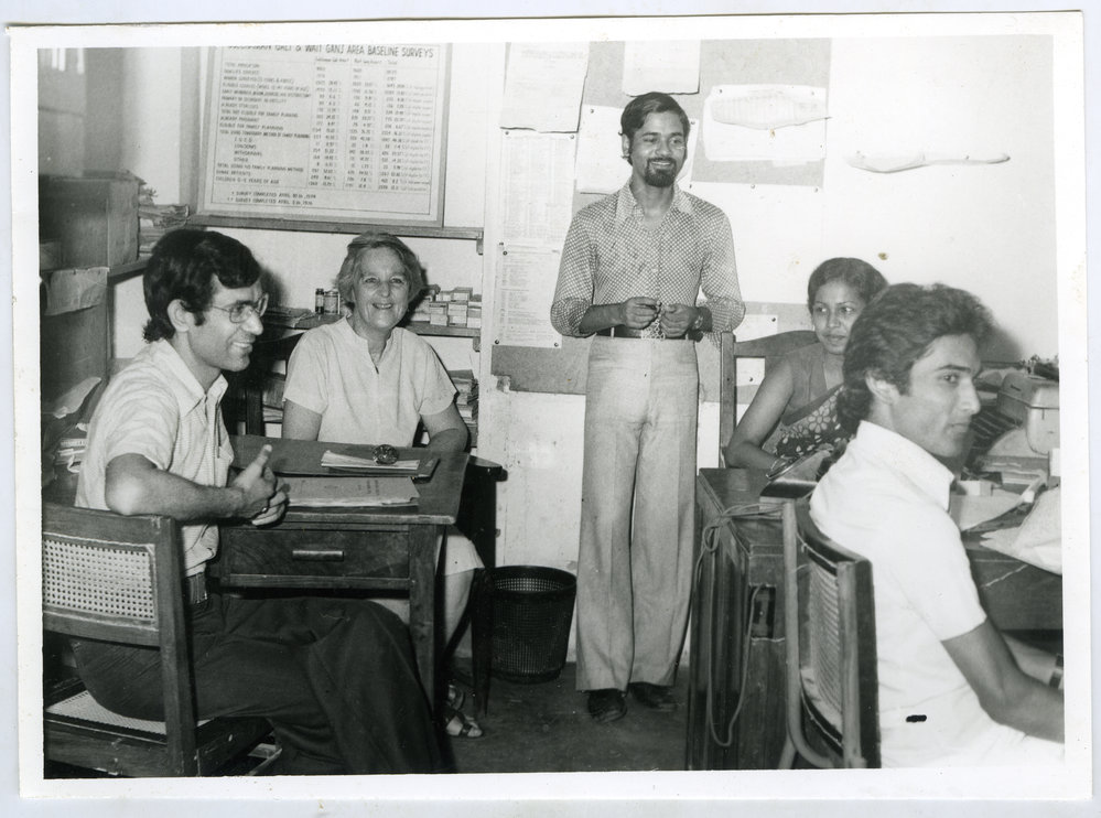 Beryl Howie seated at a desk in an office space, with three unidentified men and one unidentified woman
