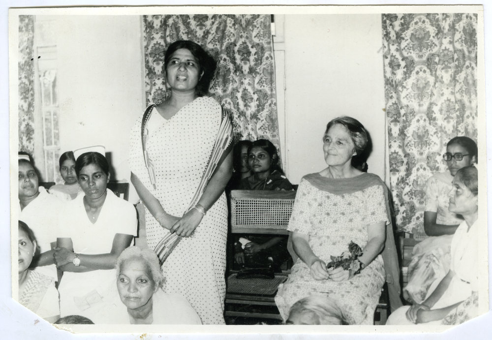 Beryl Howie is seated with other Indian women, as an unidentified Indian stands, offering a speech, Ludhiana