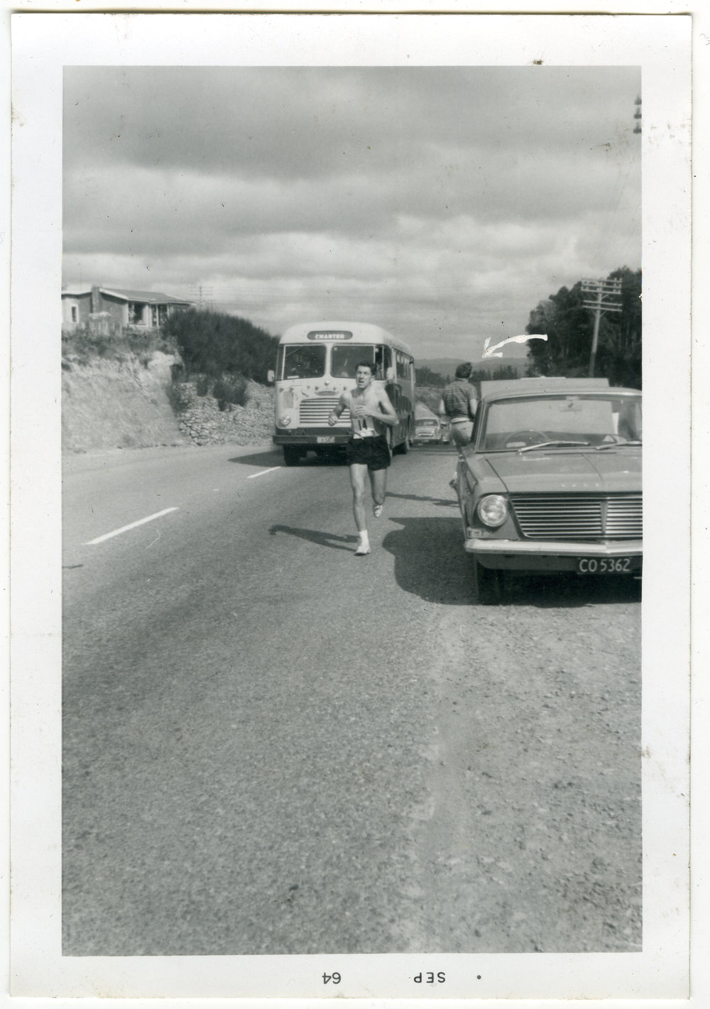 "Malcolm Shaw pursued by the Club bus at the top of Kaitoke Hill," Masterton Relay, 1964, Presbyterian Harrier Club - Wellington