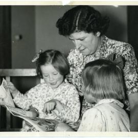 Residents of Nisbett Cottage, Glendining Home are read a bedtime story by Miss Halies, 1955