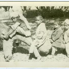 Four unidentified children sitting on a log