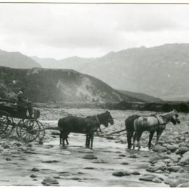 Four horses pull a coach through a stream