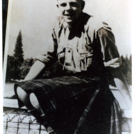 Unidentified boy wearing a kilt, sits on a metal fence 