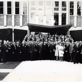 Large group of unidentified individuals standing in front of a brick building