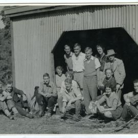 A group of unidentified men and women seated around an entrance to a barn