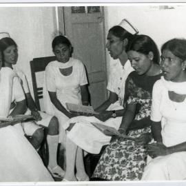 Six unidentified Indian women are seated in a circle, reading a pamphlet, Ludhiana