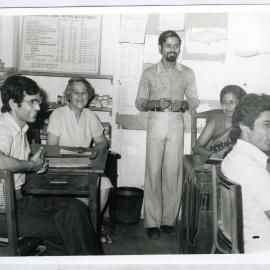 Beryl Howie seated at a desk in an office space, with three unidentified men and one unidentified woman