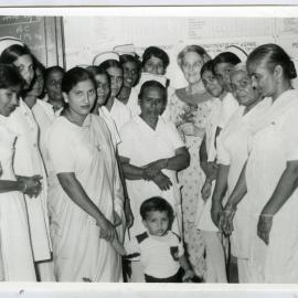 An unidentified child is photograph surrounded by unidentified female nurses and patients